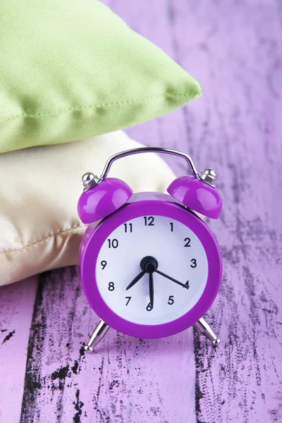 Plastic clock on a silk pillows on wooden purple background — Stock Photo, Image