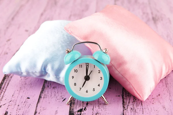 Plastic clock on a silk pillows on wooden background — Stock Photo, Image