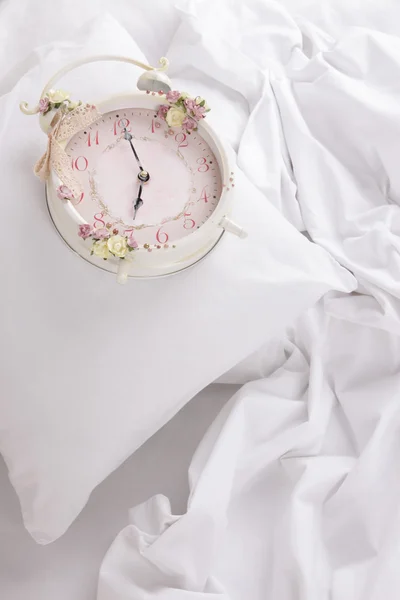 Relógio de metal em travesseiros em uma grande cama branca — Fotografia de Stock