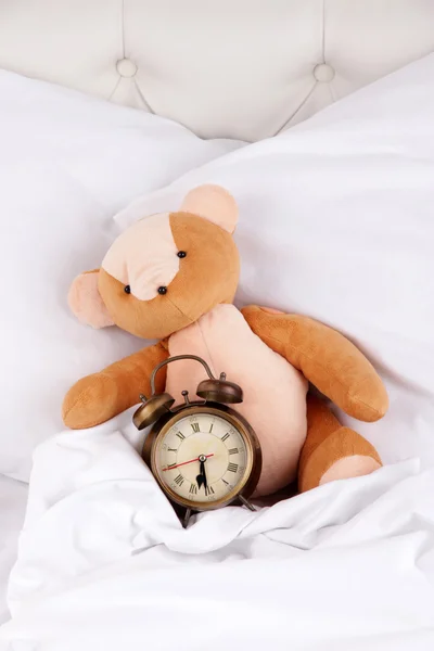 Relógio de metal e urso de brinquedo em travesseiros em uma grande cama branca — Fotografia de Stock