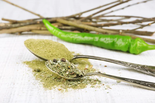 Colheres de metal cheias de diferentes temperos e ramos e pimenta perto deles em fundo de madeira branca — Fotografia de Stock