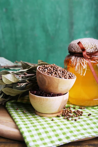 Taças de madeira redondas de tempero, folhas de louro e uma garrafa de vidro de mel em um guardanapo verde em uma bandeja em fundo de madeira — Fotografia de Stock