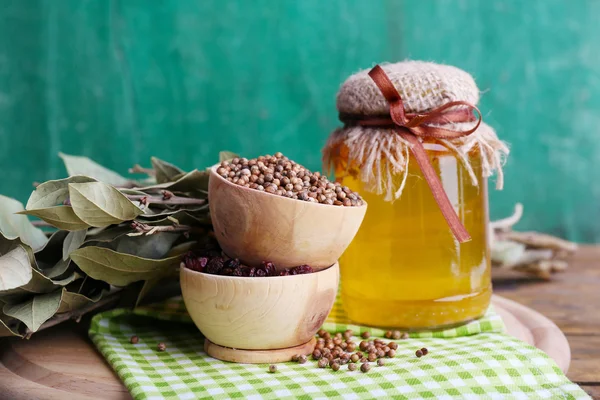 Rund trä skålar av kryddningen, lagerblad och en glasflaska honung på en grön servett på en bricka på trä bakgrund — Stockfoto