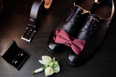 Erkek ayakkabıları, papyon, kemer ve yaka çiçekleri ahşap arka planda, fotokopi alanı. Modern erkek aksesuarları. Düğün detayları. Üst manzara, düz uzanma