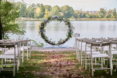 Nehir sahilinde düğün için yer, fotokopi alanı. Kemer yolunun her iki tarafında çiçekler ve sandalyelerle süslenmiş düğün kemeri. Düğün ayarları