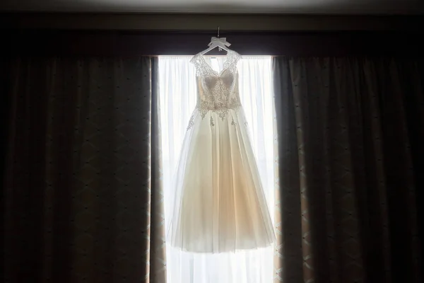コピー スペース 部屋の窓にハンガーに掛かっているベージュ刺繍のウェディング ドレスをクローズ アップ 朝の準備 — ストック写真