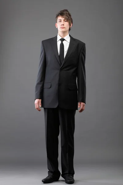 Genç işadamı gri arka plan üzerinde siyah takım elbise rahat kravat — Stok fotoğraf