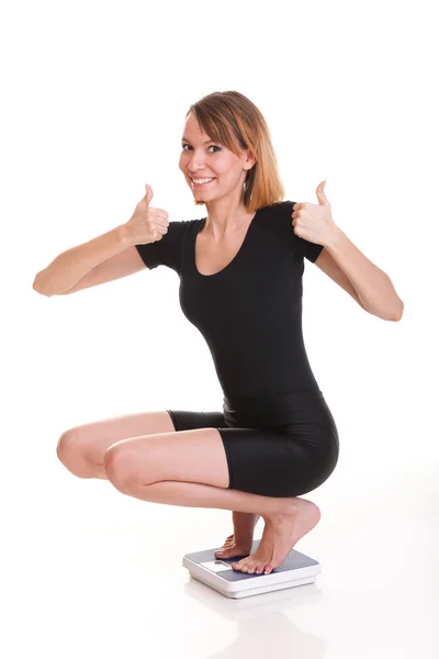 Portrait of a happy woman squatting on scales isolated — Stock Photo, Image