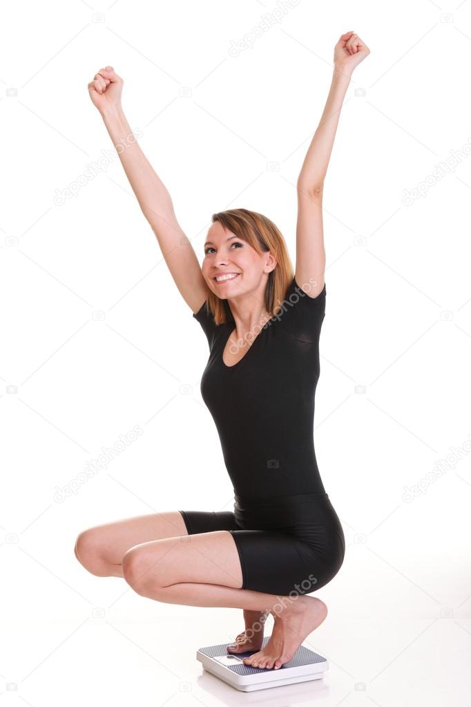 Portrait of a happy woman squatting on scales isolated