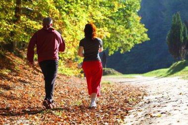 Woman and man walking cross country trail in autumn forest clipart