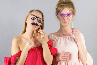 Mutlu iki kadın kağıt dekorasyon fotoğraf kabini maske gözlük ve sopa üzerinde bıyık tutan, eğlenmek. Düğün, doğum günü ve karnaval komik aksesuarlar kavramı.