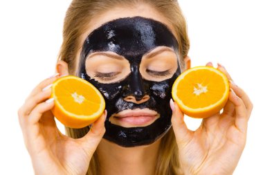 Yüzünde karbonhidrat temizleme maskesi olan ve elinde portakal meyvesi tutan bir kadın. Genç kız yağlı cildiyle ilgileniyor, gözenekleri temizliyor. Güzellik tedavisi. Cilt bakımı.