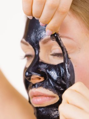 Karbonhidratlı siyah maskesini yüzünden, beyazın üstüne çıkaran genç bir kadın. Genç kız yağlı cildiyle ilgileniyor, gözenekleri temizliyor. Güzellik tedavisi. Cilt bakımı.