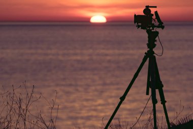 Tripod üzerindeki profesyonel kamera deniz üzerinde güneşin doğuşunu gösteren bir film çekiyor..