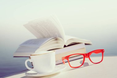 Tatillerde kitap okumak. Kahve fincanı ve kitaplar açık havada mavi deniz suyuna karşı. Kitap sayfaları rüzgarda çırpınıyor.