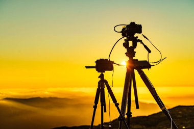 Tripod üzerindeki kamera bulutların üstünde yanan günbatımından fotoğraf çek..