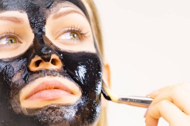 Yüzüne siyah detoks çamur maskesi süren genç bir kadın. Deriyle ilgilenen bir kız. Güzellik tedavisi. Cilt bakımı.