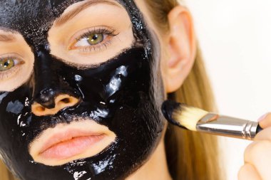 Siyah detoks detoks ile uygulanan genç bir kadın maskesini yüzüne doğru sıyırdı. Deriyle ilgilenen bir kız. Güzellik tedavisi. Cilt bakımı.