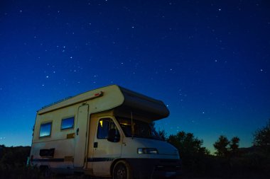 Kamp arabası karavanı yıldızlı gökyüzünün altında gece kamp yapıyor.