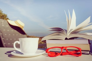 Tatillerde kitap okumak. Kahve fincanı ve kitaplar açık havada mavi deniz suyuna karşı. Kitap sayfaları rüzgarda çırpınıyor.