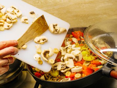 Lezzetli akşam yemeği yemek yapma. El karışık sebze ile sıcak tavaya taze dilimlenmiş mantar ekleyerek.