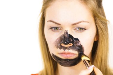 Genç bir kadın yüzünde siyah detoks çamuruyla fırça kömür maskesi takıyor. Yağlı ciltle ilgilenen bir kız. Güzellik tedavisi. Cilt bakımı.