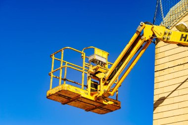 Sepet kaldırma, mavi gökyüzüne karşı inşaat alanında sarı kaldırma platformu. Endüstriyel makine, yükseklik ekipmanları üzerinde çalışıyor.