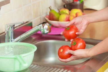 Kadın elleri mutfakta taze sebze yıkıyor su altında domates, vejetaryen salata yemeği hazırlıyor.