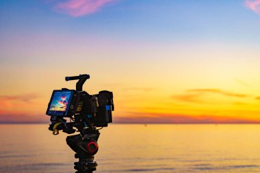 Profesyonel kamera tripodun üzerinde gün batımının görüntülerini çekiyor..