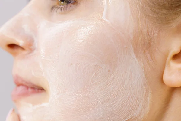 クリーム化粧品を持つ若い女性 彼女の顔にマスク水分 美の治療だ スキンケアだ サイドビュー — ストック写真