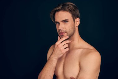 Yakışıklı bir adam. Büyüleyici genç adam, elini çenesinde tutuyor ve gülümsüyor koyu mavi arka planda dururken.