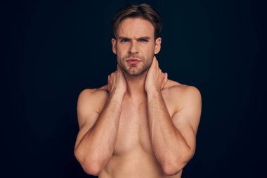 Handsome young bearded man isolated. Topless muscular man in towel is standing on dark blue background. Serious man looking at camera.