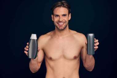 Yakışıklı genç adam izole edilmiş. Üstsüz kaslı adamın portresi elinde şampuanla koyu mavi arka planda duruyor. Erkekler kavramı önemser