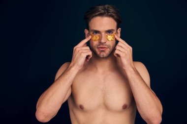 Gülümseyen, sakallı, 20 'li yaşlarda, mükemmel ciltli, göz altı nemlendirici bantlar takan, pembe arka plan stüdyosundaki çeneye destek olan genç bir adam. Cilt bakımı sağlık kozmetik prosedürleri kavramı.