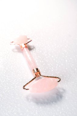 Beyaz zemin üzerinde doğal kuvars taşından yapılmış pembe yüzlü masajcı. Evde kaldırma ve tonlama tedavisi.