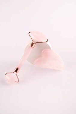 Pembe yüz silindiri ve beyaz arka planda doğal kuvars taşından yapılmış gua sha masaj aleti. Evde kaldırma ve tonlama tedavisi.