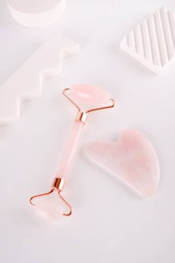 Pembe yüz silindiri ve beyaz arka planda doğal kuvars taşından yapılmış gua sha masaj aleti. Evde kaldırma ve tonlama tedavisi.