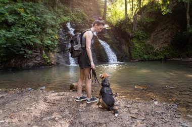 Şelalenin yanında köpeği olan genç bir kadın.