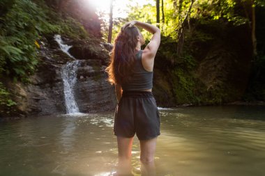 Genç bir kadın şelalenin yanında duruyor.