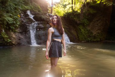 Genç bir kadın şelalenin yanında duruyor.