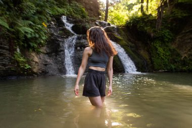 Genç bir kadın şelalenin yanında duruyor.