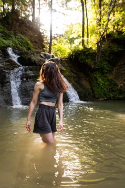 Genç bir kadın şelalenin yanında duruyor.