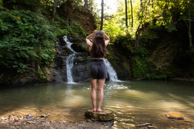 Genç bir kadın şelalenin yanında duruyor.