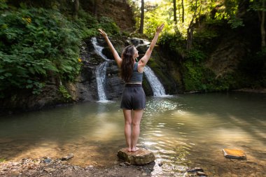 Genç bir kadın şelalenin yanında duruyor.