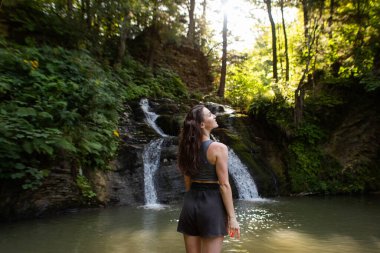 Genç bir kadın şelalenin yanında duruyor.