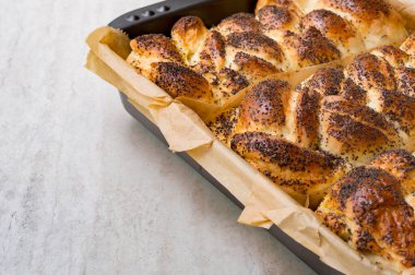 Fırında haşlanmış hasır çörekler ve haşlama kabında haşhaş tohumları. Fırın ürünleri, hamur işleri, fırınlanmış çörekler masanın üzerinde. Yemek pişirme konsepti..