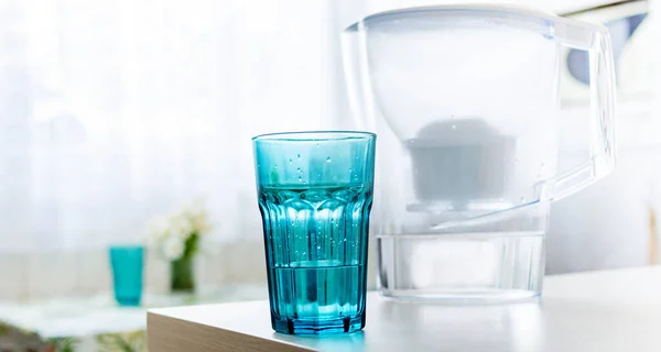 Glass of filtered water. Water filter with soft focus and flowers with soft focus on the background. Healthy Lifestyle. Ecology.