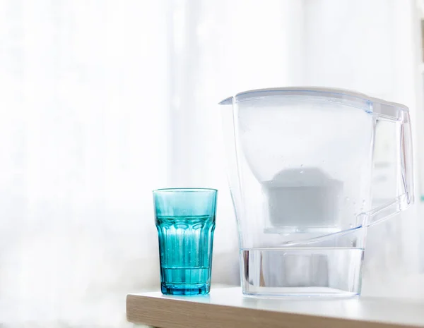 Water filter jug and blue glass with water on light blurred background. Healthy lifestyle. Ecology.