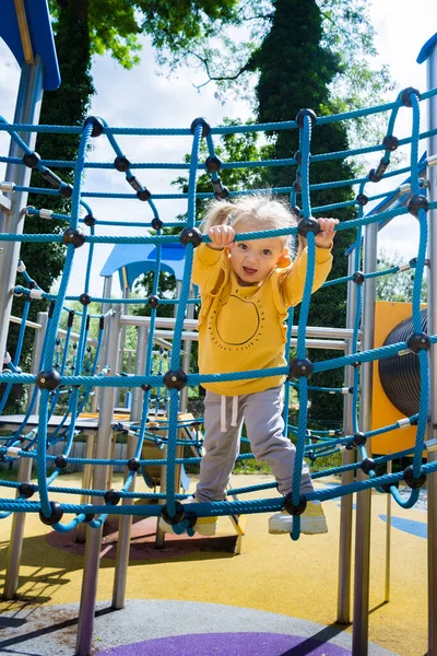 little girl in a yellow sports sweater playing on the playground. Emotions of happiness, fun, joy.