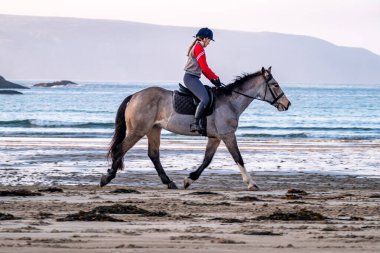 BURTONPORT, İLK DONEGAL, IRELAND - 18 ARALIK 2021: Patricia Ward sahilde atına biniyor